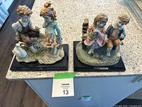 Photo showing two charming ceramic figurines of children on blackwood rectangular bases, set on a kitchen counter.