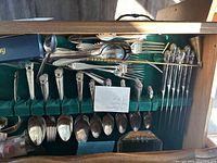 Boxed silverware set with intricate ornate designs on handles. Includes multiple types of forks, spoons, and knives arranged in a green velvet-lined tray.