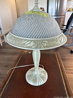 Full view of the ceramic table lamp showing the embossed floral design on the shade and base, the slender stem, and pull chain switch.