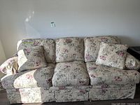 Full view of floral patterned sofa bed with three seat cushions and matching floral throw pillows.