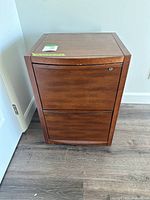 Front view of a mahogany wood file cabinet with two drawers and a lock on the top drawer.