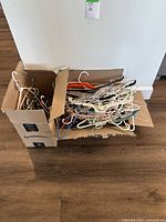 Two boxes filled with assorted clothes hangers, including metal wire, plastic, and velvet-coated types in various colors.
