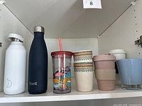 Full shelf view showing seven assorted drinkware items including S'well bottles, patterned tumblers, and cups