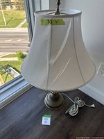 Full view of the lamp showing white fabric shade and metal base with decorative details.