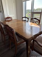Dining table with 6 chairs around it in a room with sunlight showing wear on the table surface.