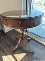 Side view of the round wooden side table showing the drawer and pedestal base with brass-capped feet.