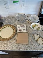 Photo showing all pieces on the kitchen counter, includes clear glass bowls, ceramic trivets, and plates with floral and decorative patterns