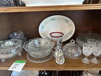 Shelf display with various glass and ceramic pieces including bowls, plates, stemmed glasses, and salt and pepper shakers with floral details