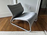 Side angle showing the curved tubular chrome frame and stretched silver fabric seat with wear at edges.