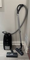 AEG Vampyr TC 350 black canister vacuum cleaner with hose, telescopic wand, main vacuum head attached and an additional vacuum head on floor in corner