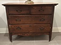 Front view of antique wooden dresser showing four drawers with metal handles, castors on legs, and visible wood grain.