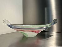 Side profile of an art glass candy bowl showing translucent glass with green and red swirls and pinched ends forming textured handles.