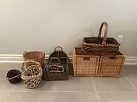 Photo showing seven varied baskets arranged on the floor against a wall, including storage baskets and decorative baskets in different sizes, shapes, and styles.