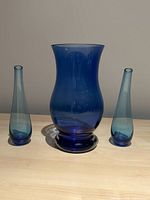 Three blue glass vases arranged with one large central vase and two smaller curved vases, photographed against a neutral background to show shape, color, and condition.
