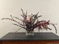Front view of faux plant arrangement in clear ribbed glass vase with marbles