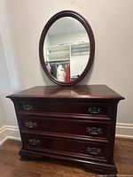 Front view of the mahogany dresser with oval mirror in a room showing wood grain and details of metal drawer pulls.