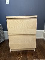 Front view of the nightstand showing both drawers closed, highlighting light wood grain finish and minimalistic design.