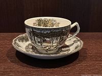 View of Johnson Brothers tea cup and saucer with a winter village ice house pattern on a wooden shelf.