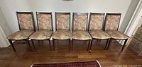 Front view of six MCM style dining chairs in a row, showing floral upholstery and rosewood finish.