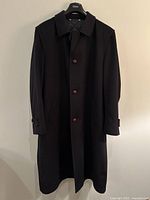 Front view of black men's long coat by Steinbock showing collar, brown buttons, and side pockets.