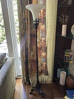 Full view of the black metal standing lamp with frosted glass shade located next to curtain and window, showing the base and upper light fixture.