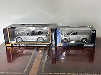 Photo of the two model cars in original boxed packaging on a dark surface, showing front and side view.
