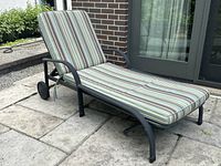 Side view of adjustable patio lounge chair with cushion on patio stones showing wheels and armrests.