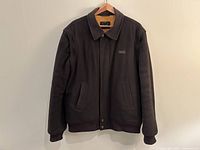 Front view of the brown Paul & Shark bomber jacket with collar and snap buttons, hanging on a wooden hanger.