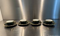 Group of four matching green and gold cups on saucers lined up
