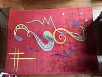 Top-down photo of red area rug with colorful abstract squiggle pattern on wooden floor.