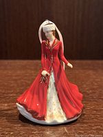 Front view of Royal Doulton Hallelujah Chorus Christmas ornament figurine, showing detailed red coat and white dress with gold accents, white hanging ribbon, and holly sprig in hand.