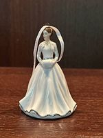 Close-up of the front side of the Royal Doulton ceramic Christmas tree hanging figurine ornament showing the full white flowing dress and face details with white hanging ribbon.