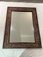 Full view of the rustic wooden hanging mirror showing the carved floral pattern frame and the clear mirror surface on a white quilted background.