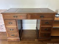 Front view of antique style desk showing wood finish, simulated leather inlaid top, and drawer handles.