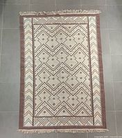 Full view of the Southwest style area rug laid flat on a tiled floor, showing pattern and fringe.
