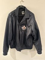 Front view of navy blue Toronto Marlies leather jacket hanging on hanger showing logo patch