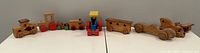 Wide shot of all wooden toys including trains, cars and airplane spread in a line on a table.