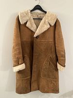 Full front view of vintage Morelands shearling coat hanging on a black hanger against white background, showing tan lambskin exterior with cream shearling collar and cuffs.
