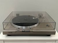 Front view of turntable with dust cover closed showing platter and control buttons