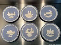 Top-down view showing six blue Wedgwood Jasperware plates with white relief landmarks of London, arranged two rows of three on a metallic surface.