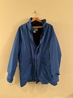 Front view of blue Woolrich Teton Gore-Tex jacket hanging, showing full length with front flap pockets and folded collar.