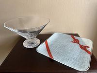 Clear crystal decorative bowl with textured base alongside square plate with red ribbon pattern shown on table.