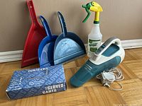 Lot arranged on wooden floor showing red and blue dustpans, box of gloves, spray bottle, and Black & Decker Dustbuster vacuum with charger