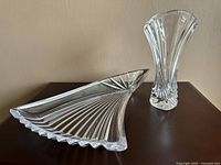 Side angle of the crystal plate showing fan-like ribbed design and scalloped edge, with the tall crystal vase beside it.