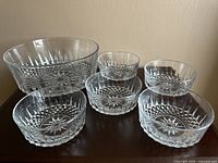 Photo showing one large serving bowl and six small matching bowls, all made of cut glass with an elegant patterned design.