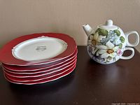 Stacked red Bistrot salad plates with floral porcelain teapot stacked with matching cup on top