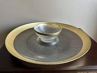 Full view of the chip and dip set with a large round plate and smaller bowl showcasing textured glass and gold rim.