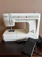 Full side view of white Kenmore sewing machine with foot pedal on table beside it.