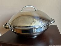 Photo of the complete stainless steel wok with matching lid placed on top, showing wide bowl and handles.