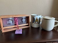 Photo showing two etched glass tumblers with maple leaf design in wooden box, ceramic mug with colorful 'DAD' text, and white ceramic tea mug with lid.